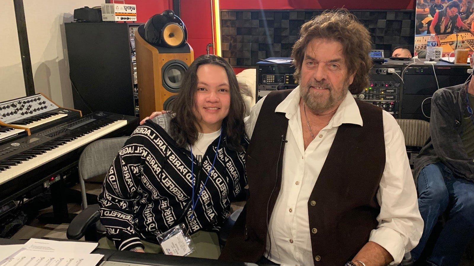 Alan Parsons sits with Steffie Tj和ra in front of a mixing board in a recording studio. They are smiling at the camera.