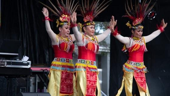 三个女人戴着五颜六色的印尼羽毛头饰跳舞, yellow skirts, and beaded belts and collars.