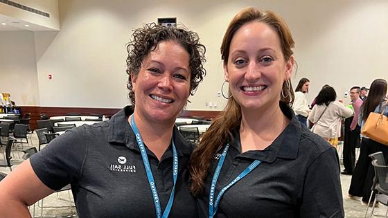 Michelle Moreno and Stacie Aldrich smiling and standing side by side wearing blue lanyards with conference badges and black 满帆 polo shirts.