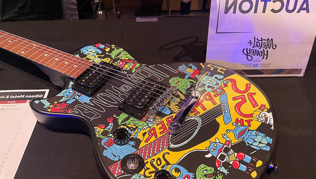 The body of a black electric guitar with a colorful graphic appliqué next to a sign that reads “silent auction.”
